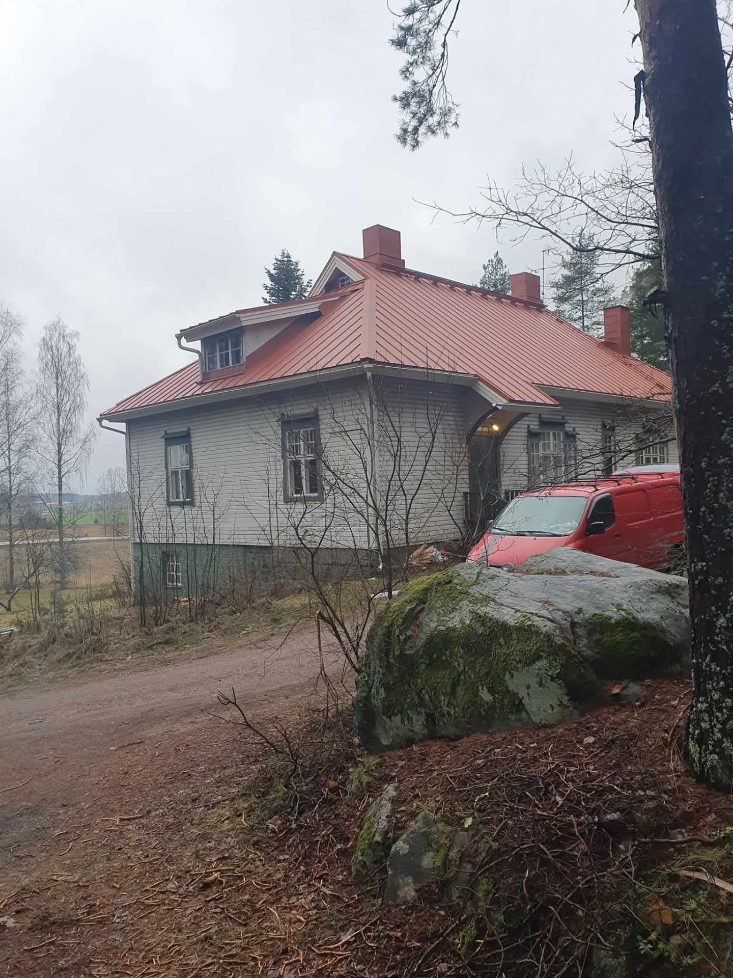 Vanha puutalo oranssinpunaisella peltikatolla, punainen pakettiauto pihassa