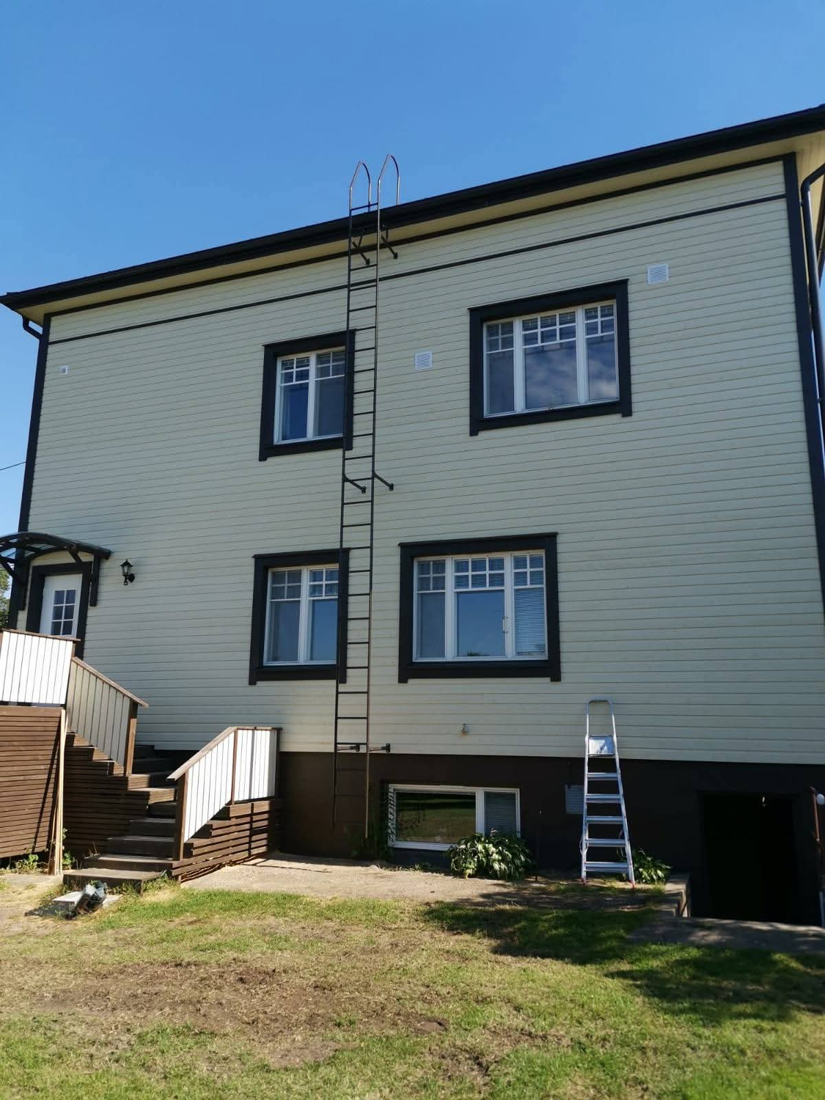 Vaalea julkisivulaudoitus mustilla ikkunanpuitteilla ja kiinteillä tikkailla