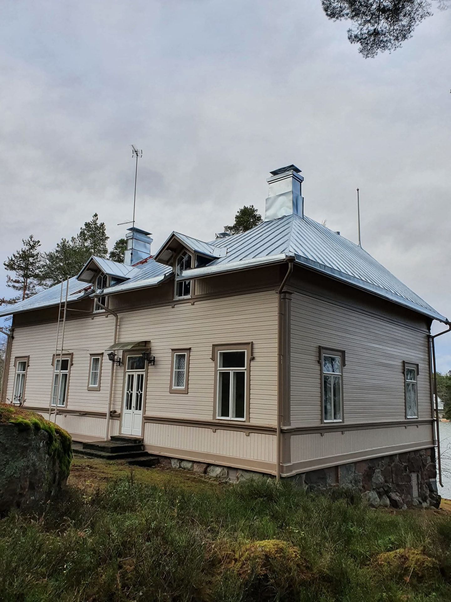 Vaalea puuhuvila harjakattoisella peltikatolla kallion päällä